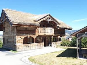 At the end of summer, under a vast blue sky, Chalet Ker Béla built from ancient wood, its terraces, and the gazebo in the garden.