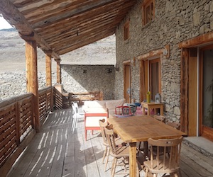 La gran terraza cubierta construida en madera maciza de la casa rural Ancolie y los muros de piedra en pleno verano.